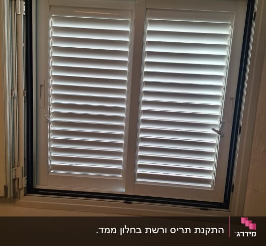 חלון אלומיניום לבן עם תריס הזזה ידני המותקן בחלון ממ"ד
